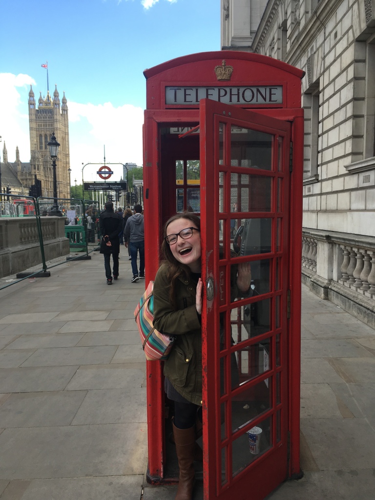 Young woman stands in a red telephone box outside Westminster Station in London, England, UK